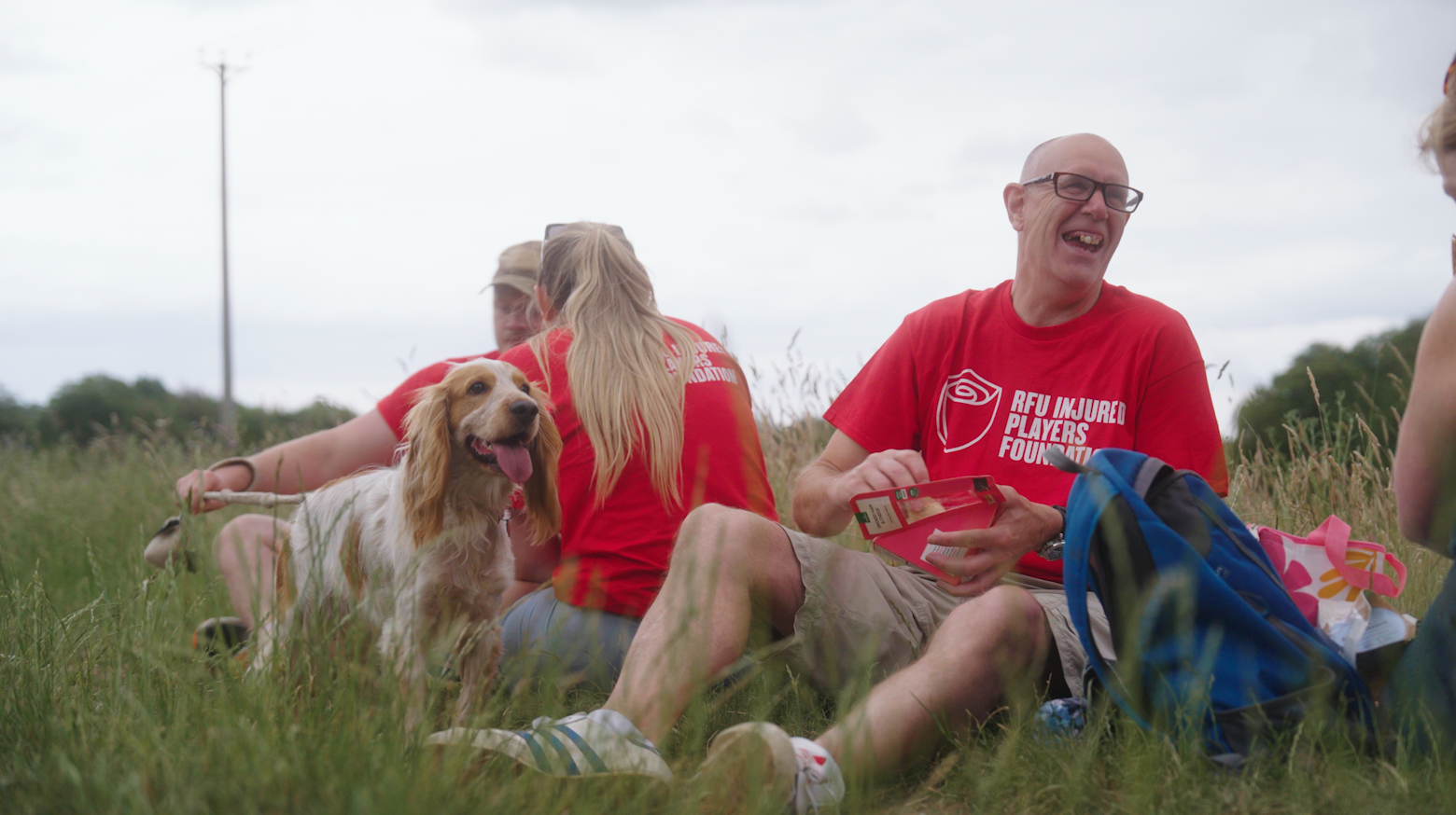 group of people on hike sat eating lunch with dog